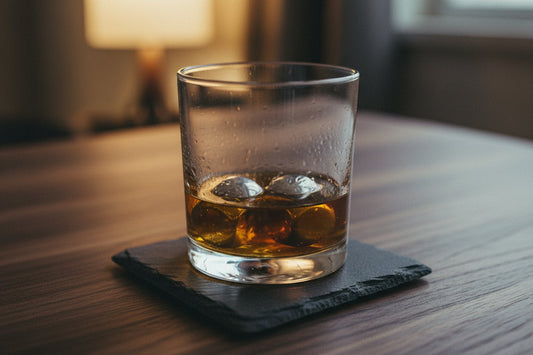 Glas med whisky og polerede stålterninger på en skiferbrik